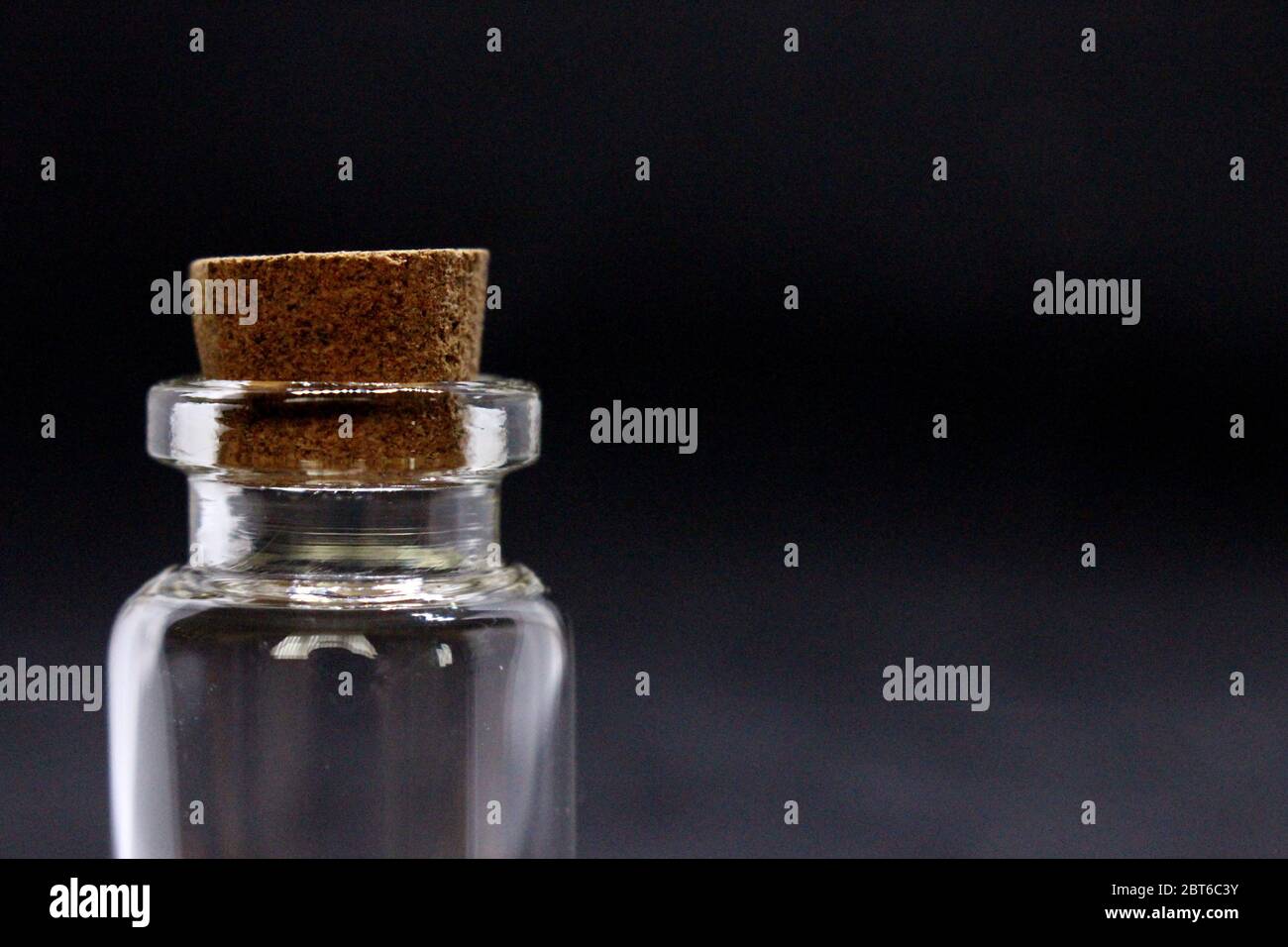 A close up photograph of one empty glass bottles with cork stopper, against a black background Stock Photo