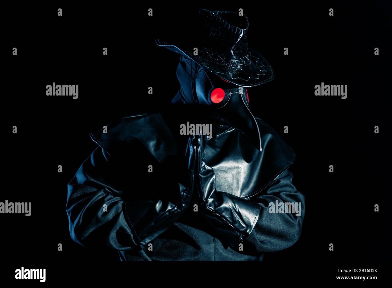 Man in plague doctor costume with crow-like mask praying with hands ...