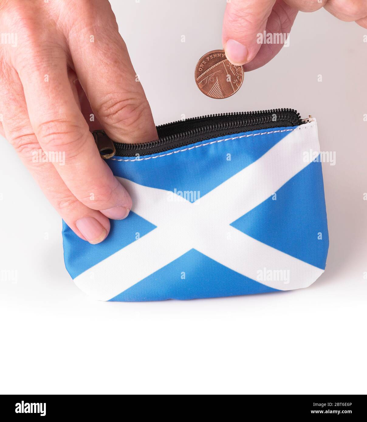 Hand placing British one penny coin into Scottish Saltire flag purse Stock Photo