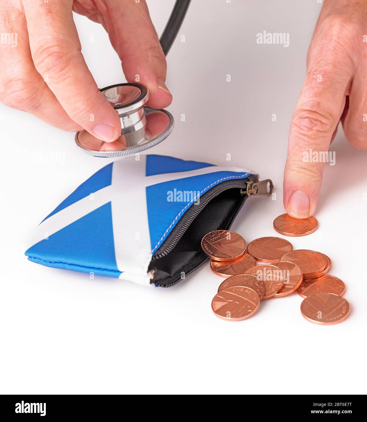 Hand holding stethoscope to Scottish Saltire flag purse with coins spilling out Stock Photo