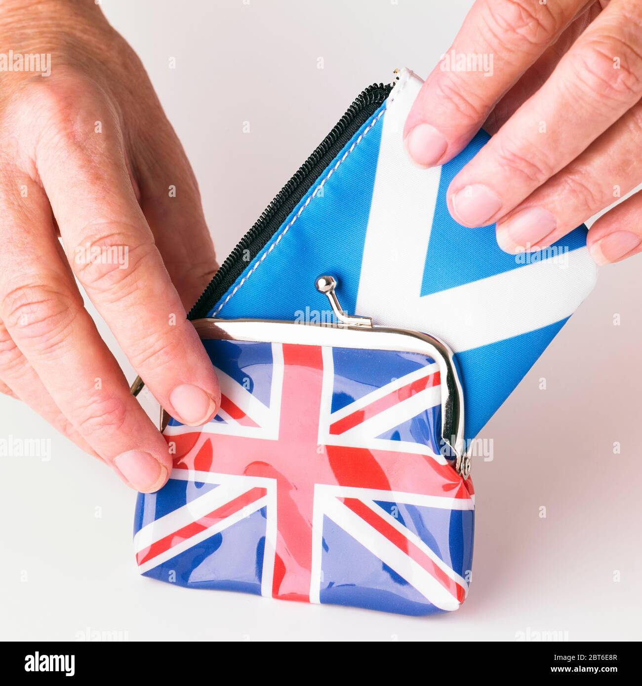 Hands forcing larger Scottish purse into smaller Union Flag purse Stock Photo