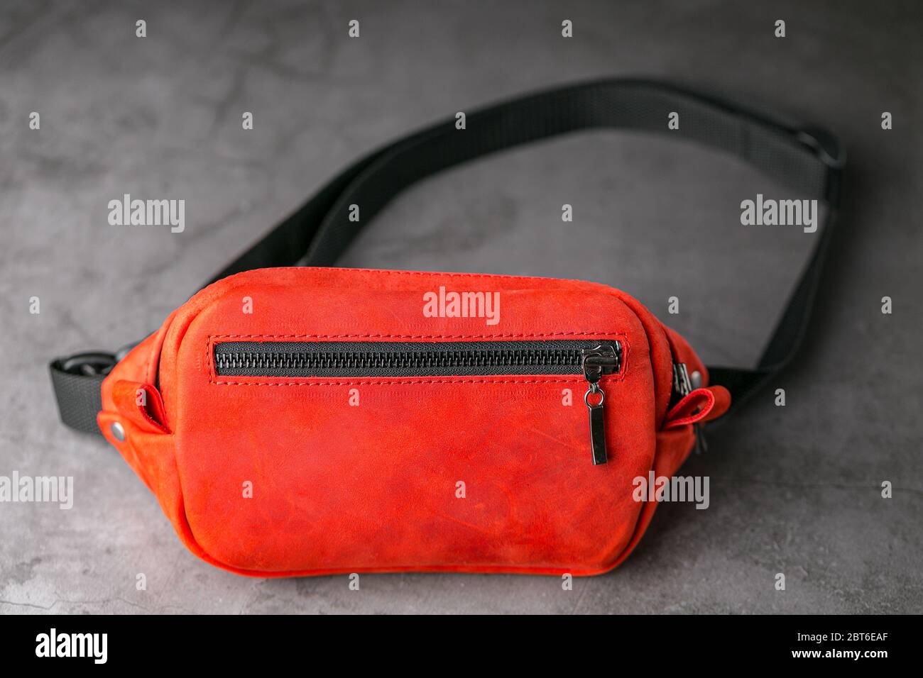 Red waist bag made of leather, banana on a gray background. Handmade