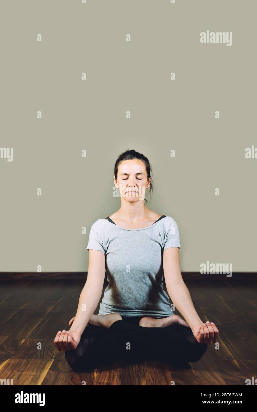 Woman sitting cross-legged on the floor doing yoga relaxation exercises. Concept of healthy living and yoga Stock Photo