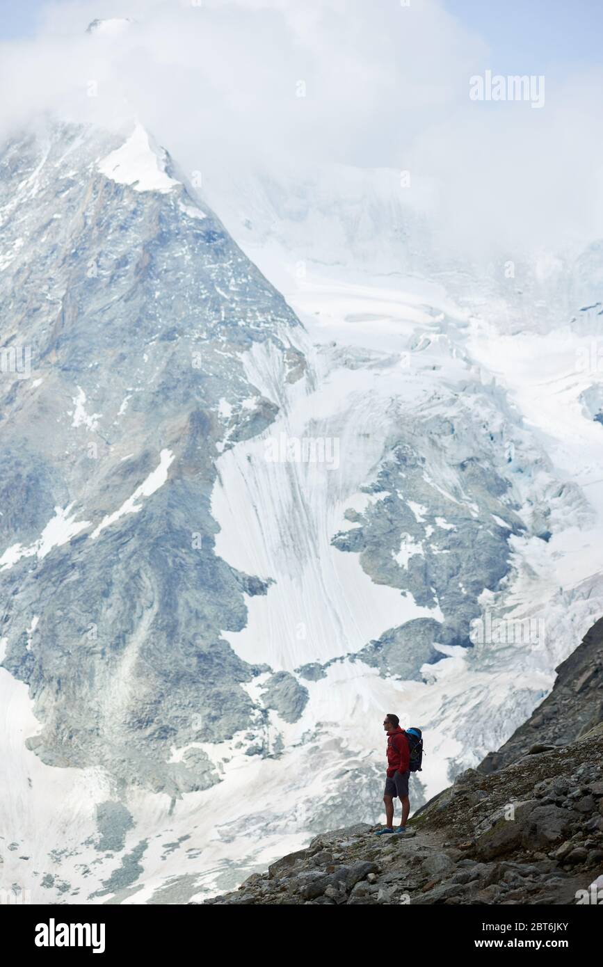 Incredibly beautiful mount in Swiss Alps - Ober Gabelhorn, male hiker with backpack standing on a slope enjoying a cold quiete scenery. Concept of freedom, mountain hiking, tourism and alpinism Stock Photo