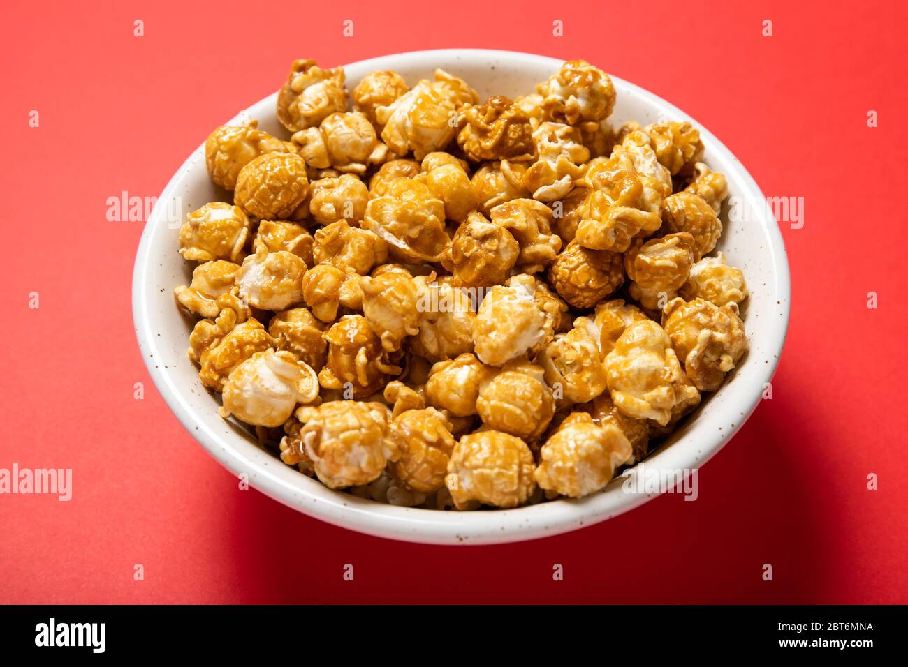 Plate with caramel popcorn on a red background Stock Photo