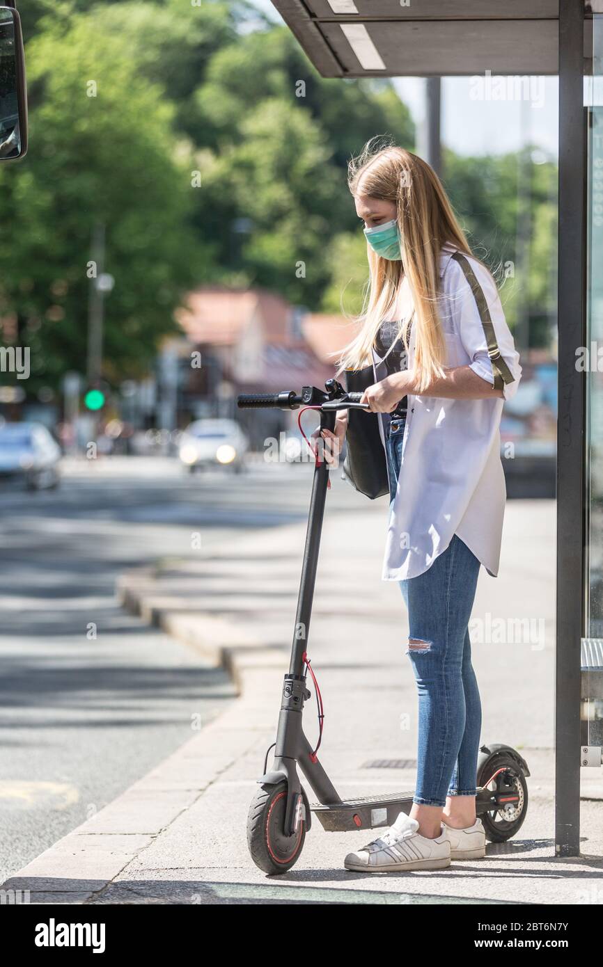 Casual caucasian teenager commuter waering protective face mask against spreading of corona virus with modern foldable urban electric scooter waiting Stock Photo