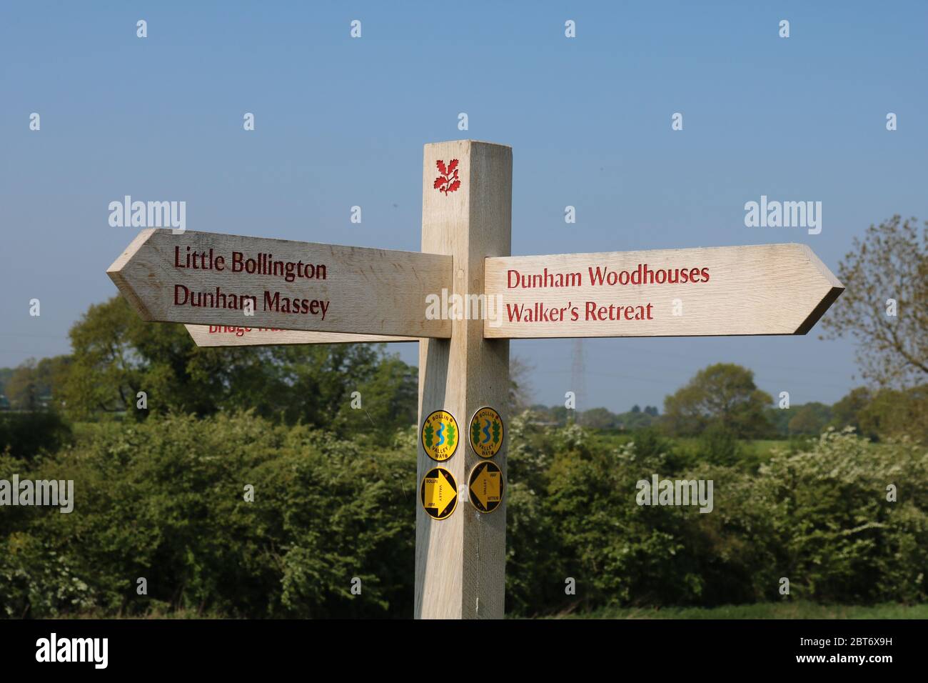 National Trust Wooden signpost showing directions to Little Bollington, Dunham Massey, and Dunham Woodhouses  with symbols for the Bollin Way Stock Photo