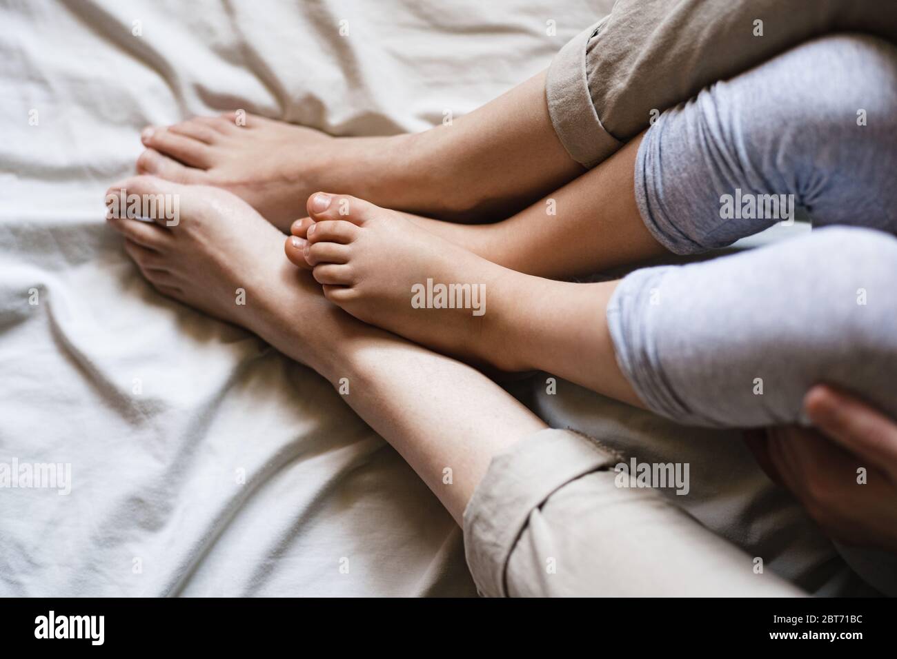 Close up of a mother and child's feet rubbing together while sitting on some beige bed sheets. It's a tender intimate moment Stock Photo