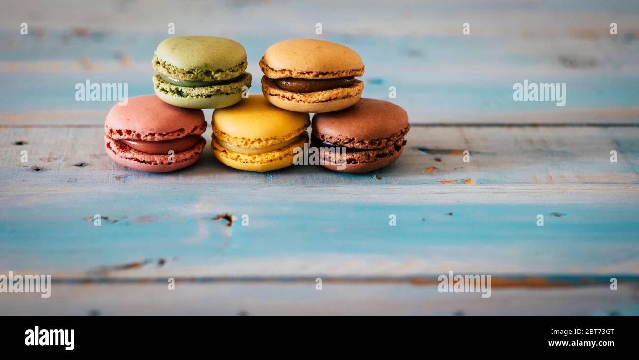 Close up of coloured and tasty hand made macarones cakes - sugar biscuits on a blue wooden trendy table - chocolatee and food energy concept Stock Photo