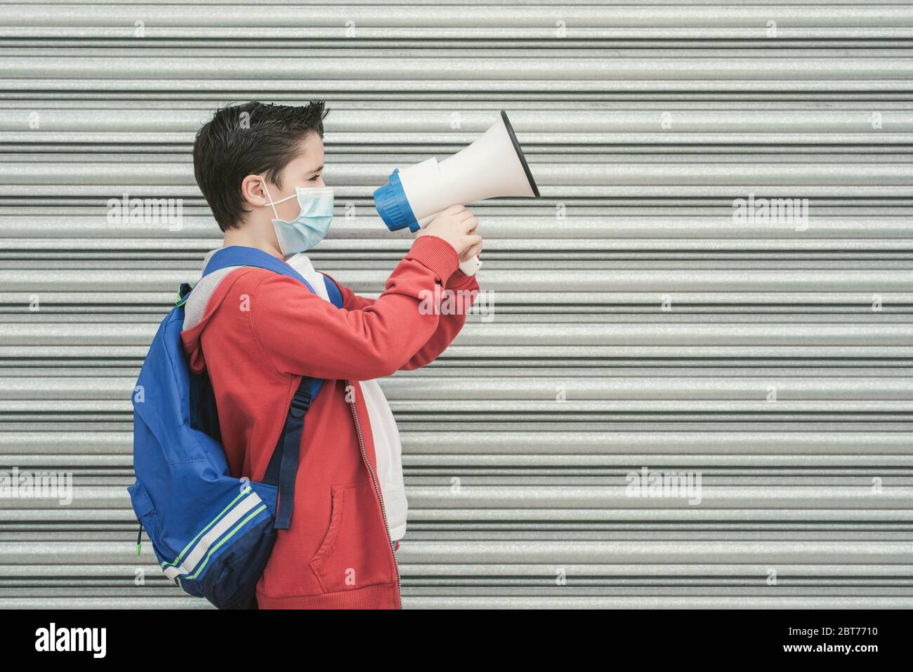 kid with medical mask and backpack screaming with megaphone back to school outdoor Stock Photo