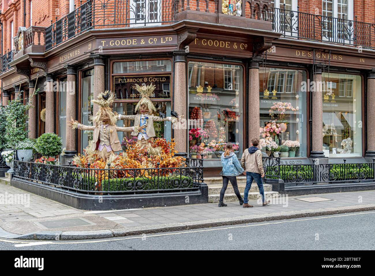 Two people walking past display of Scarecrows outside Thomas Goode & Co, a china, silverware and glass shop Mayfair, London Stock Photo