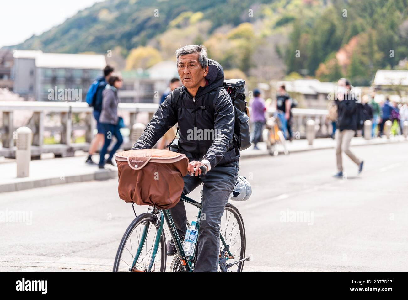 Kyoto, Japan - April 11, 2019: Arashiyama Togetsukyo Bridge with people tourists and closeup of local Japanese man riding bicycle crossing Katsura riv Stock Photo