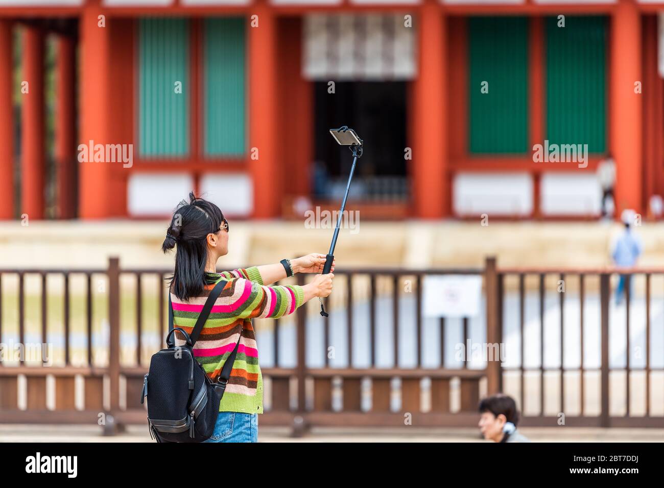 Nara, Japan - April 14, 2019: Back of people woman tourist taking picture with selfie stick of Kofuku-ji temple Chu-Kondo Central Golden Hall in city Stock Photo