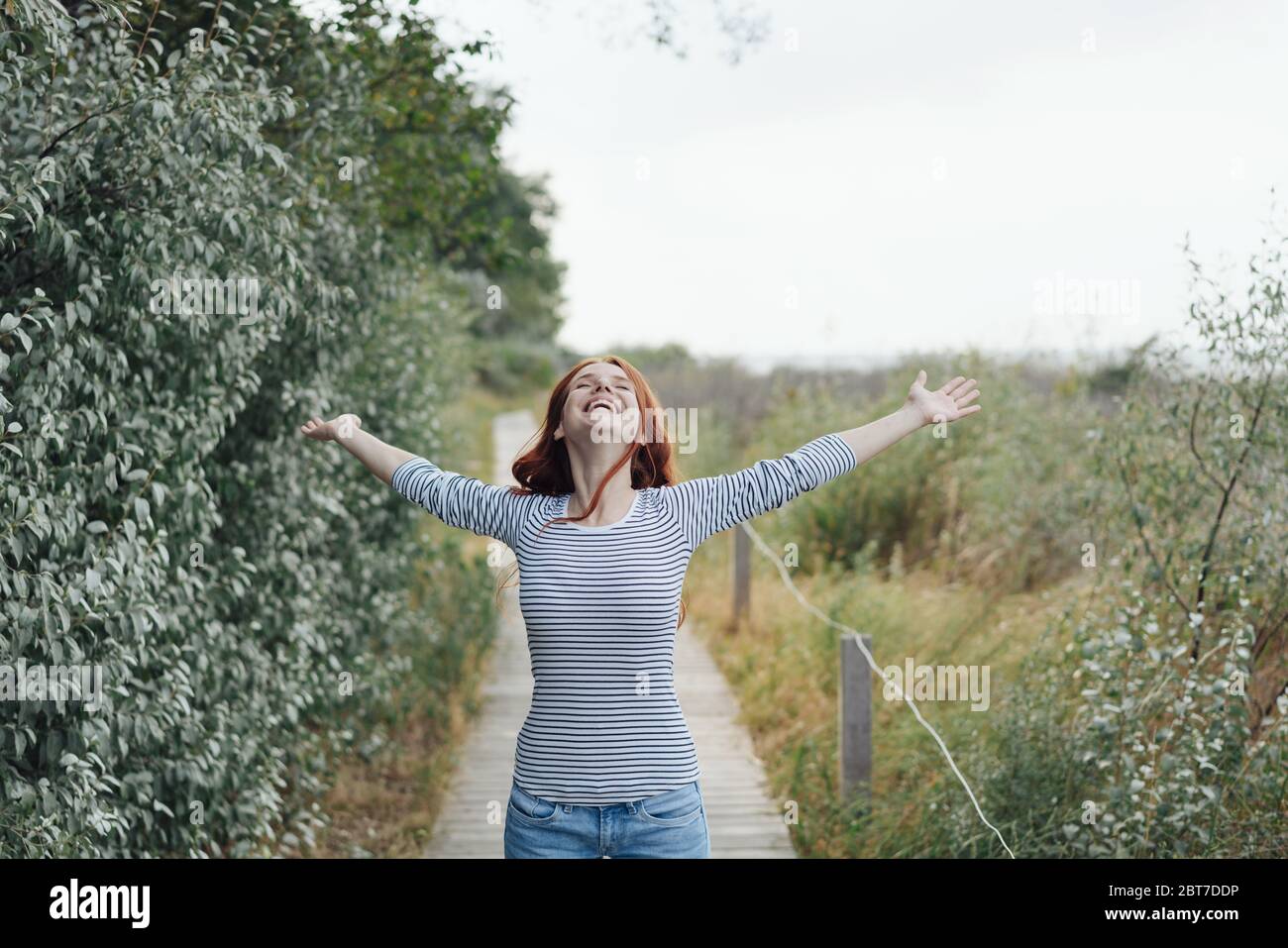 lektier klon hinanden Happy young woman celebrating being in nature walking down a wooden  boardwalk with arms out flung and head back Stock Photo - Alamy
