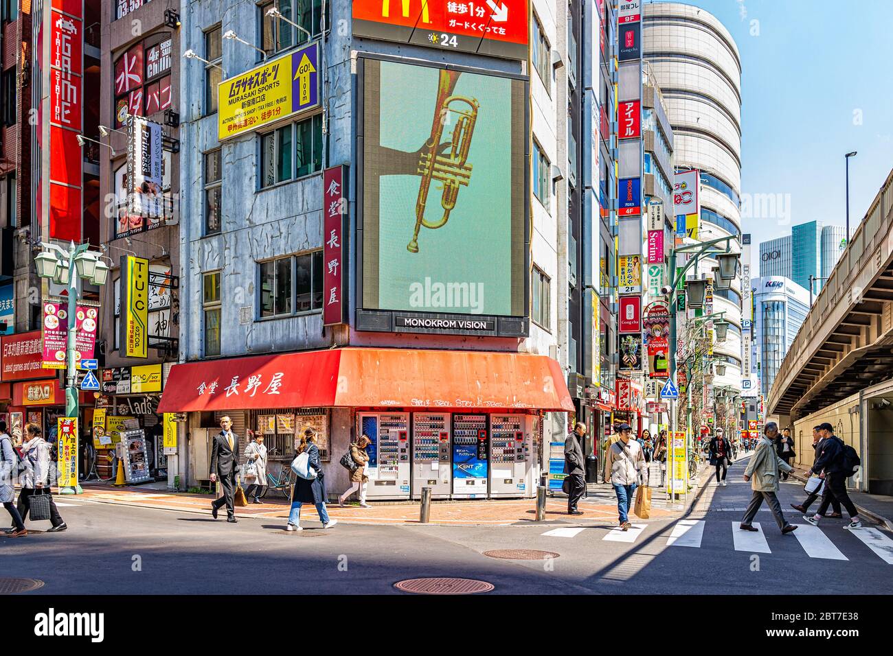 Tokyo, Japan - April 2, 2019: Shinjuku colorful red buildings with people crossing street road during day with sign for Mcdonalds fast food restaurant Stock Photo