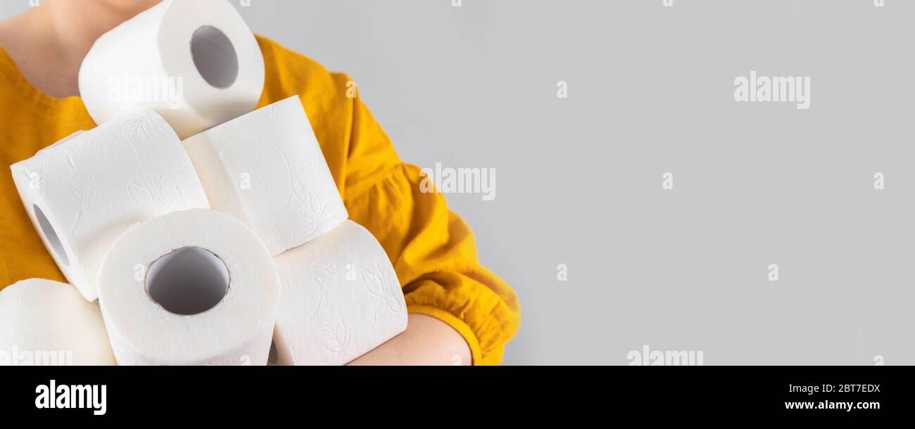 Female hands holds many rolls of toilet paper with copyspace on gray
