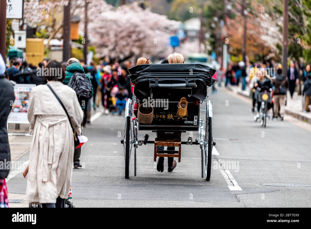 Kyoto, Japan - April 11, 2019: Arashiyama Togetsukyo Bridge street with many people tourists riding rickshaw tour walking by cherry blossom trees in s Stock Photo