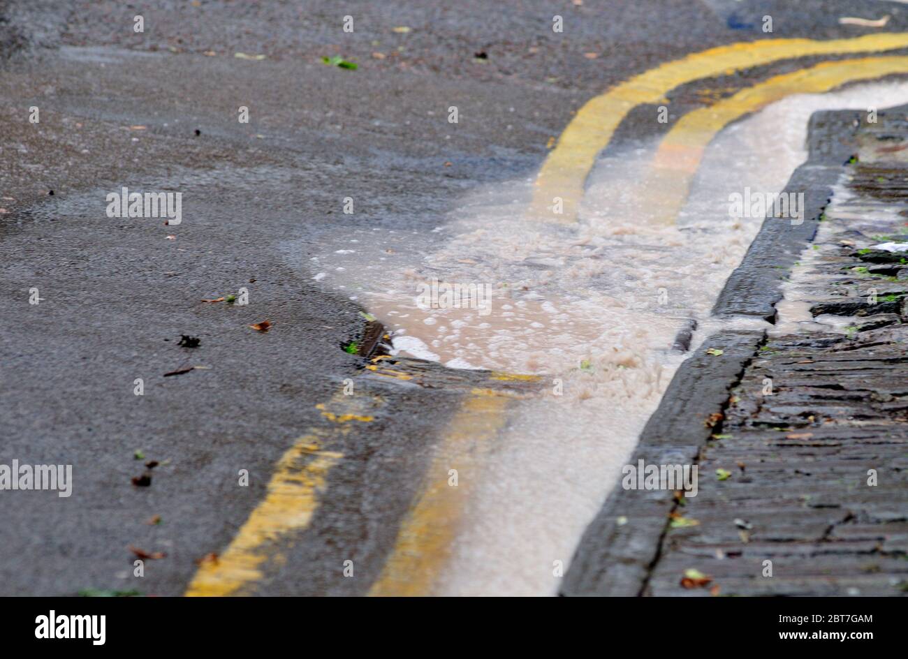 Rainwater pouring over blocked surface water road drain, UK Stock Photo