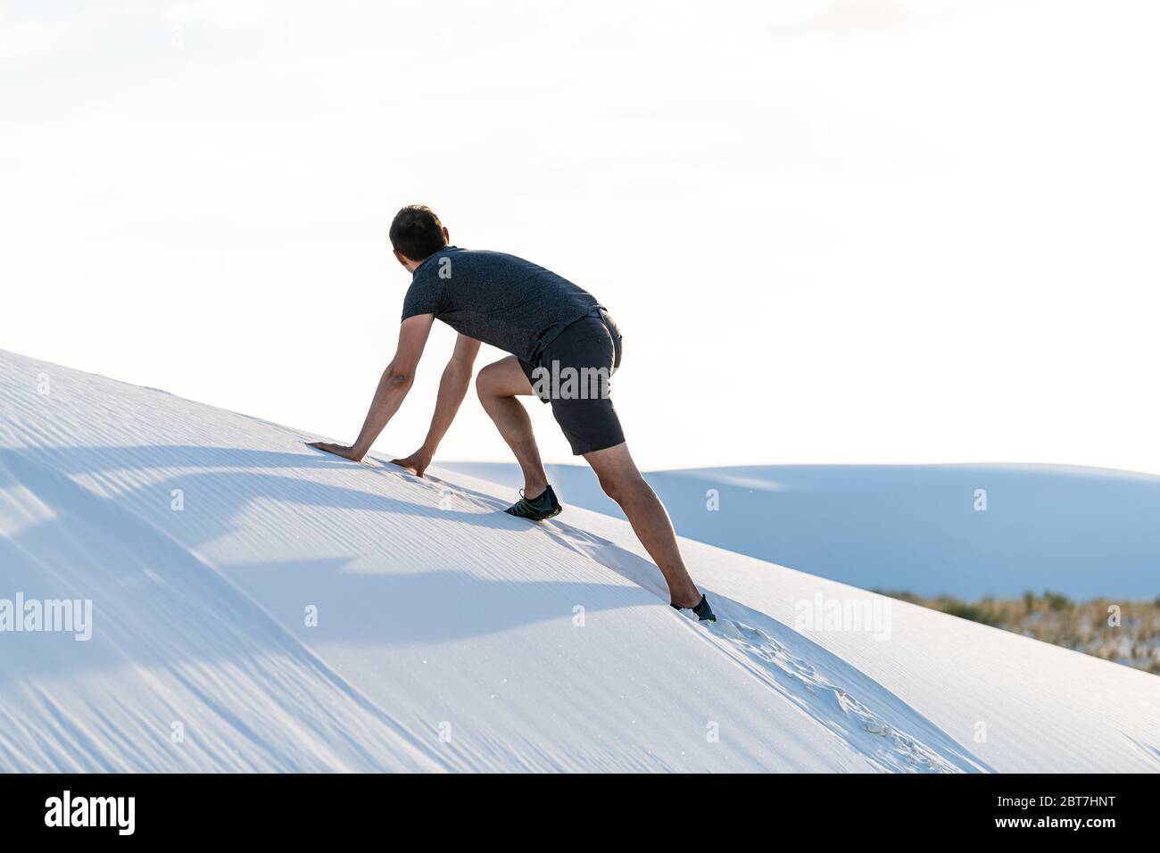 Man one person climbing on all fours on sand hill in white sands dunes national monument in New Mexico at sunset looking at view Stock Photo