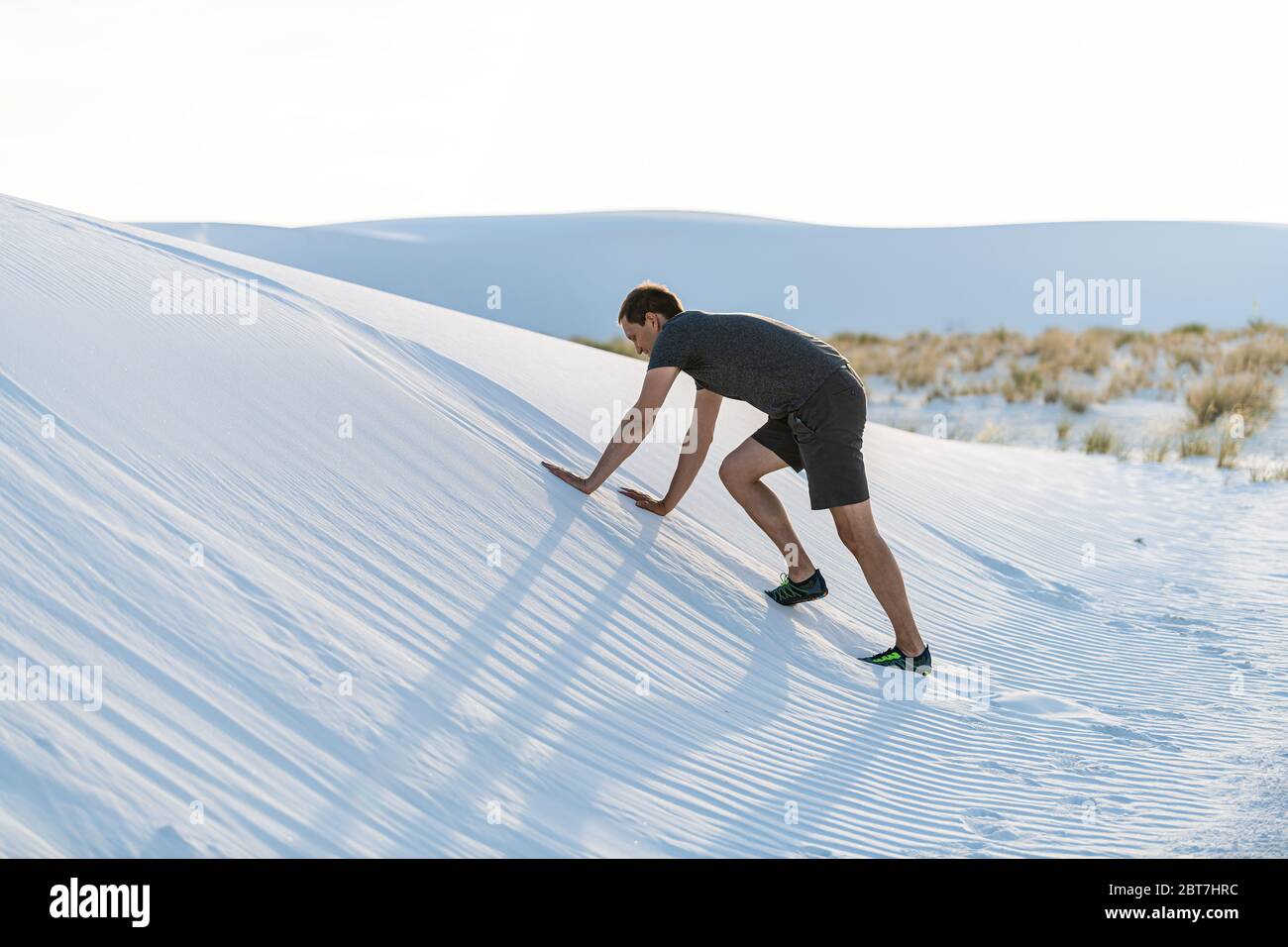 Man climbing on all fours on sand hill in white sands dunes national monument in New Mexico at sunset Stock Photo