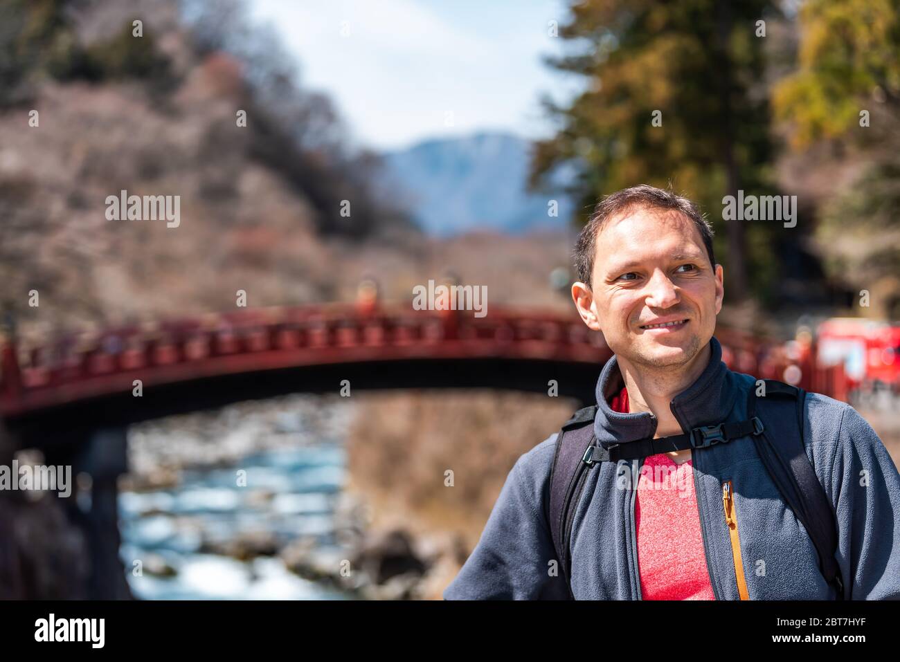 Nikko, Japan mountains and famous red bridge landmark in blurry background in Tochigi prefecture in Japan with young happy tourist man smiling Stock Photo