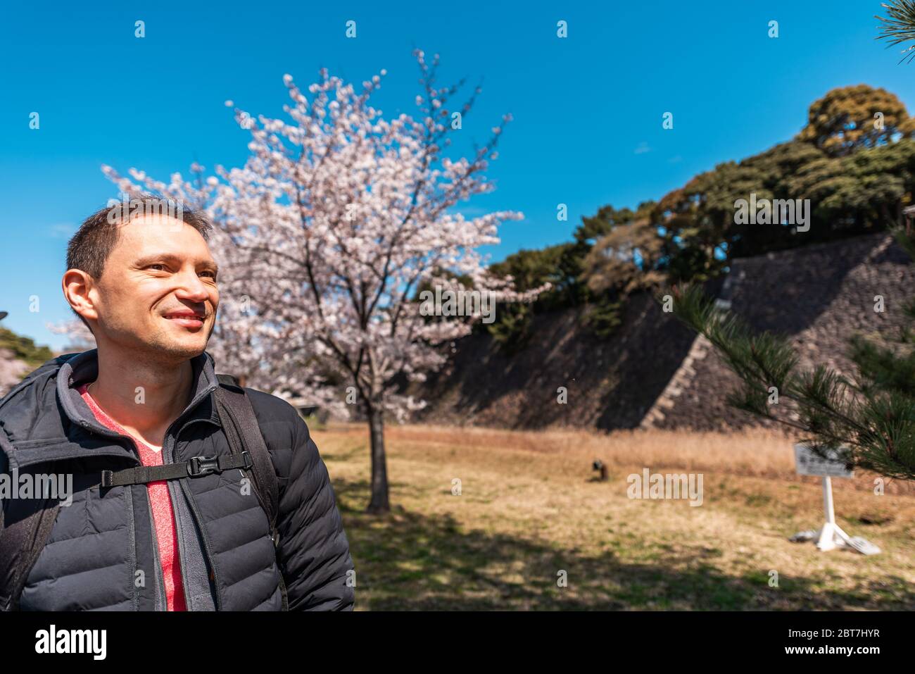 Tokyo, Japan Imperial palace national gardens park with happy tourist foreigner man by cherry blossom sakura flowers trees and wall Stock Photo
