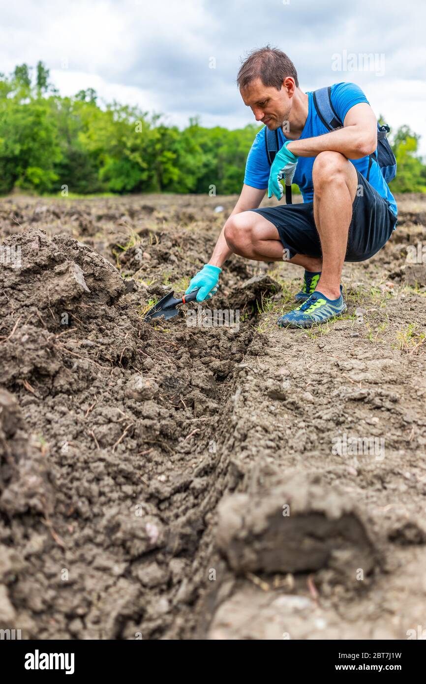 Man digging with shovel low angle view for gemstones in brown soil in Arkansas dirt landscape meadow field in Crater of Diamonds State Park Stock Photo