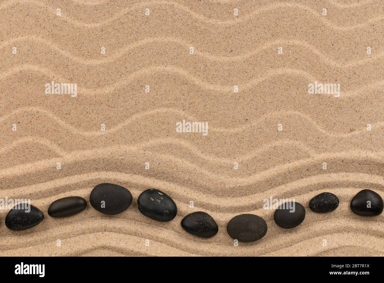 Wavy line made of black stones lying on the sand of a beach. Top view. Copy space Stock Photo