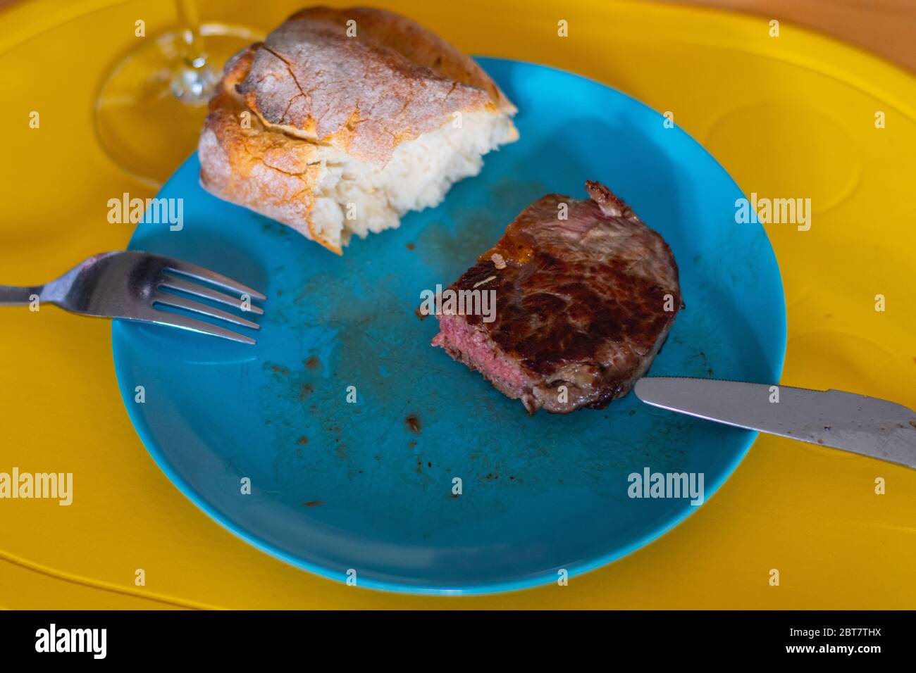 Shots of a sliced  fresh rump steak with fat on the steak on a blue plate, a glass of wine and a baguette Stock Photo