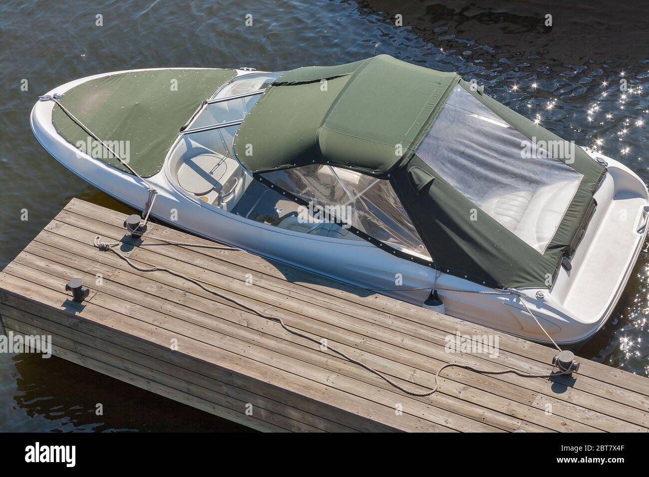 Luxury boat moored on a sunny day, view from above. Wooden pier at river with rope and mooring post. Stock Photo