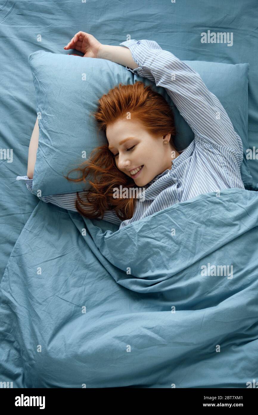 A redhaired girl in striped pajamas is lying in a blue bed stretching