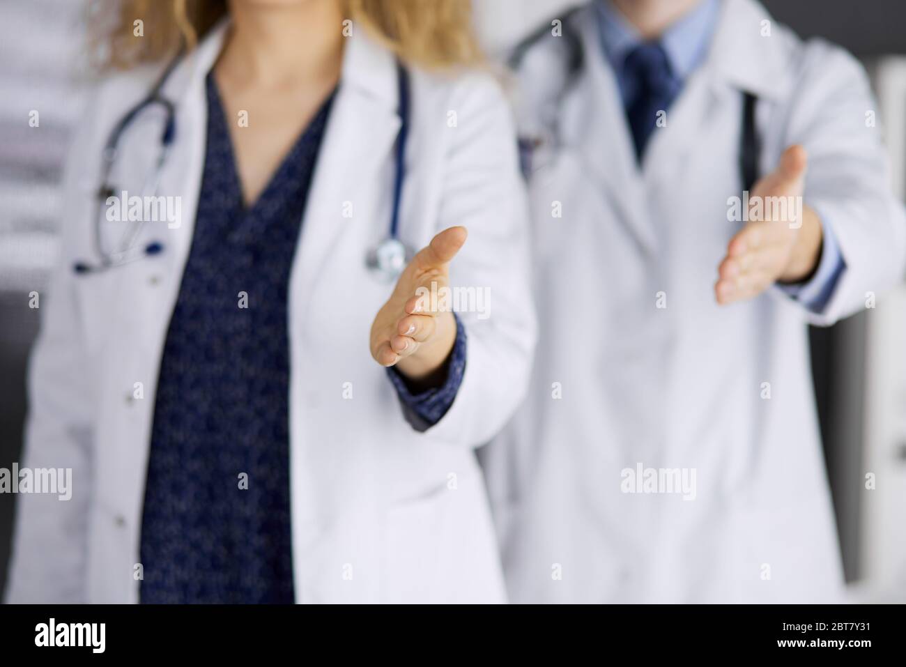 Two doctors standing and offering helping hand for shaking hand or saving life. Medical help, countering viral infection and medicine concept Stock Photo