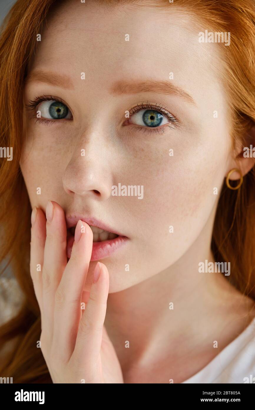 A close portrait of a beautiful red-haired girl with blue eyes. Looks into the frame and pressing his fingers to his lips Stock Photo