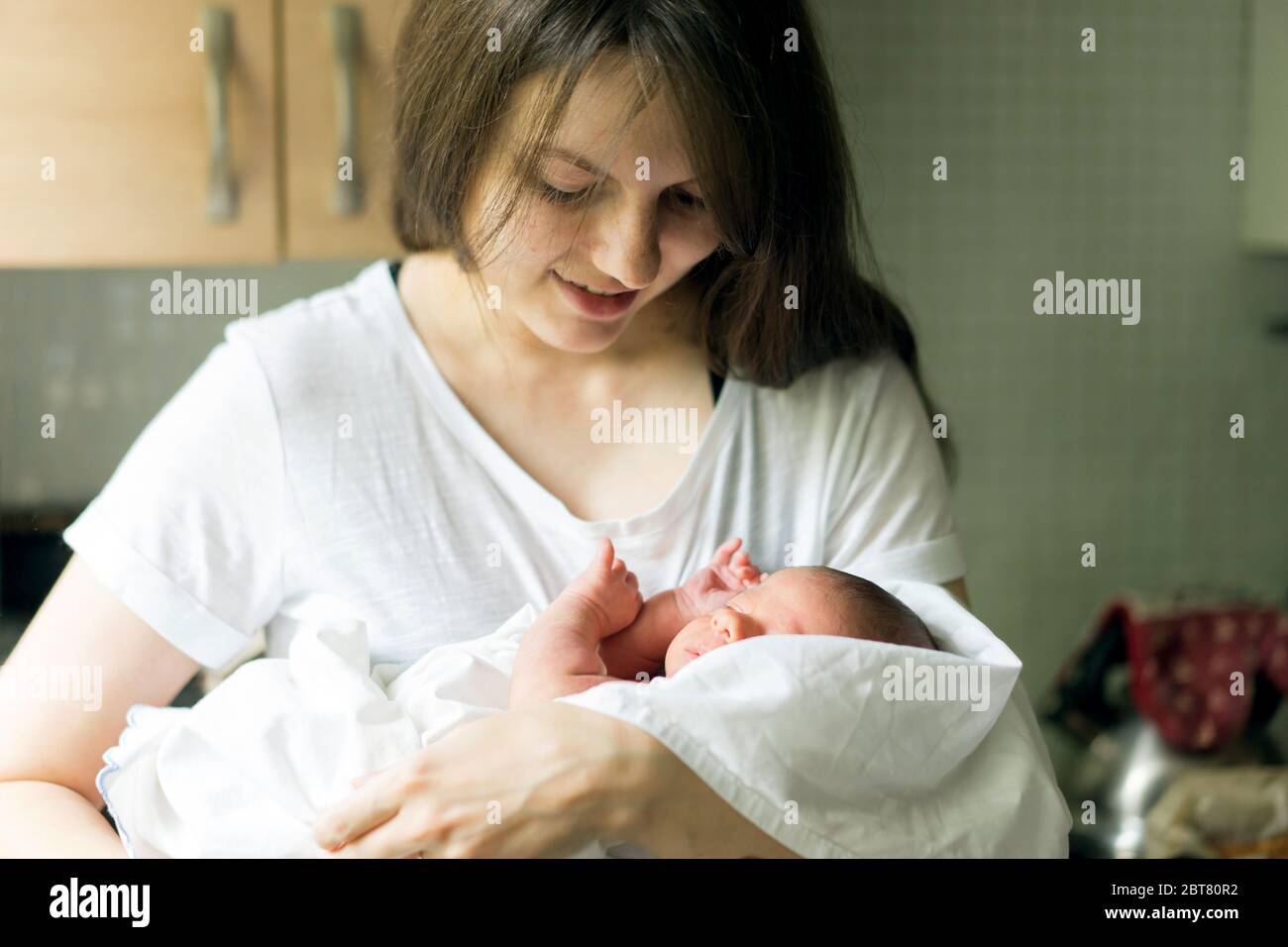 A mother with a newborn baby boy in her arms is breastfeeding him in the kitchen Stock Photo
