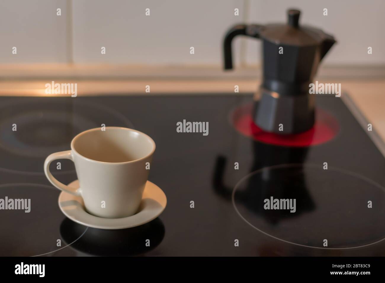 Cup of coffee on a ceramic hob and a coffee pot on an unfocused fire Stock Photo
