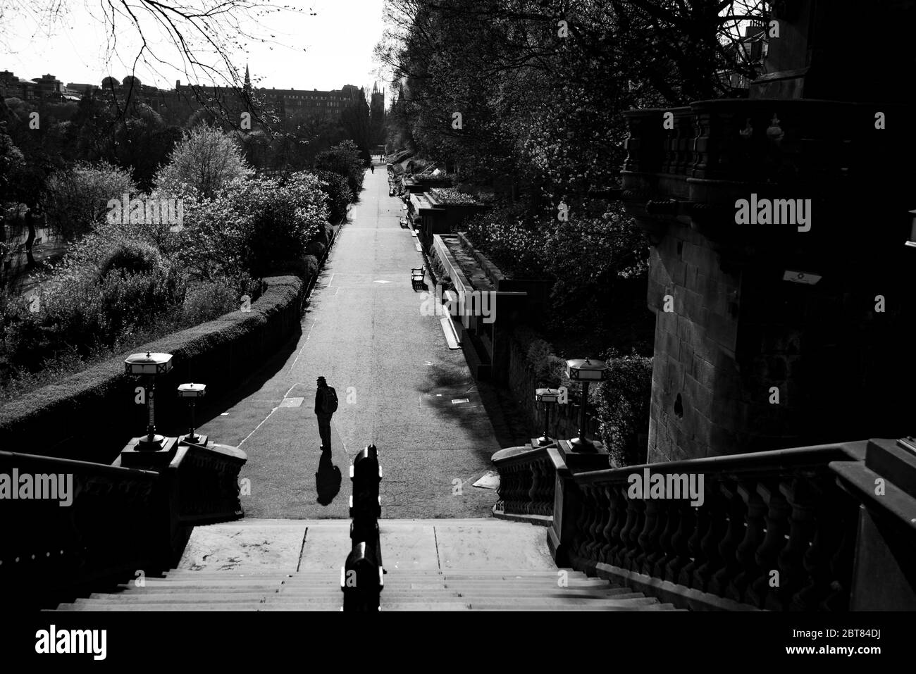 Solitary man walking towards stairwell out of a deserted Princes Street Gardens Edinburgh during lockdown 2020. Dramatic black and white shot. Stock Photo