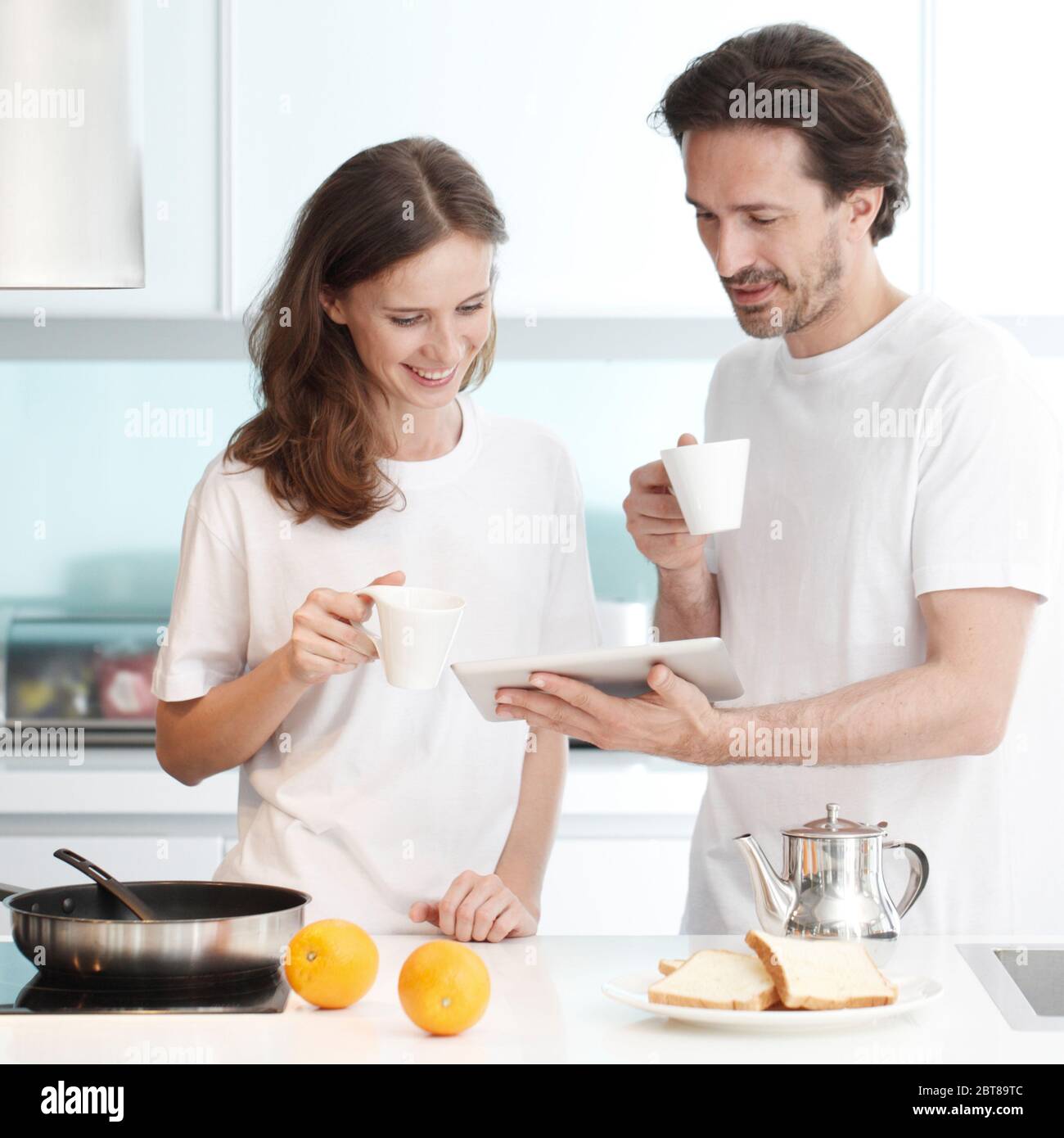 Couple cooking breakfast together in kitchen using tablet pc Stock Photo