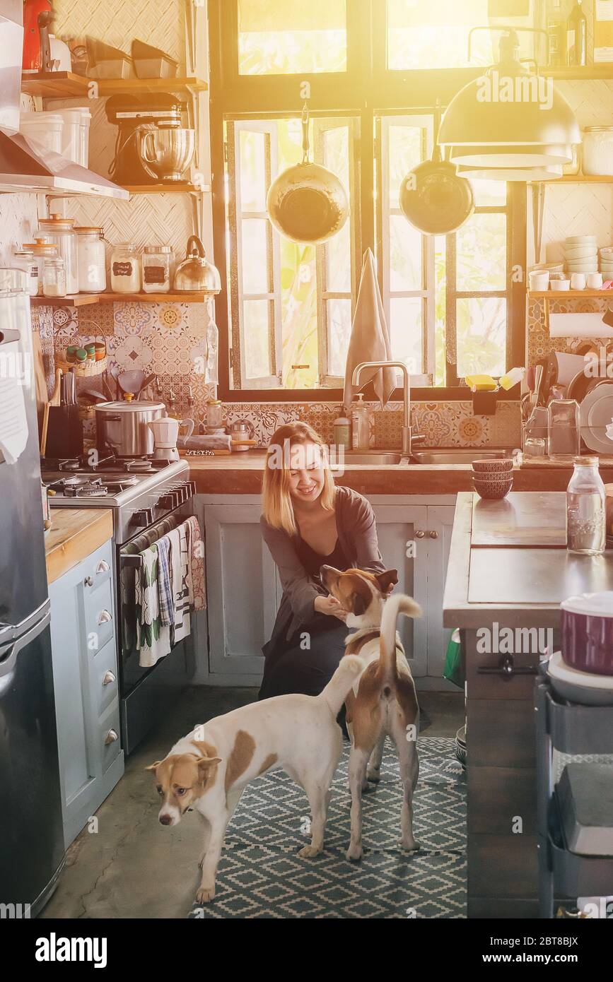 Woman petting two dogs in her old rusty kitchen Stock Photo