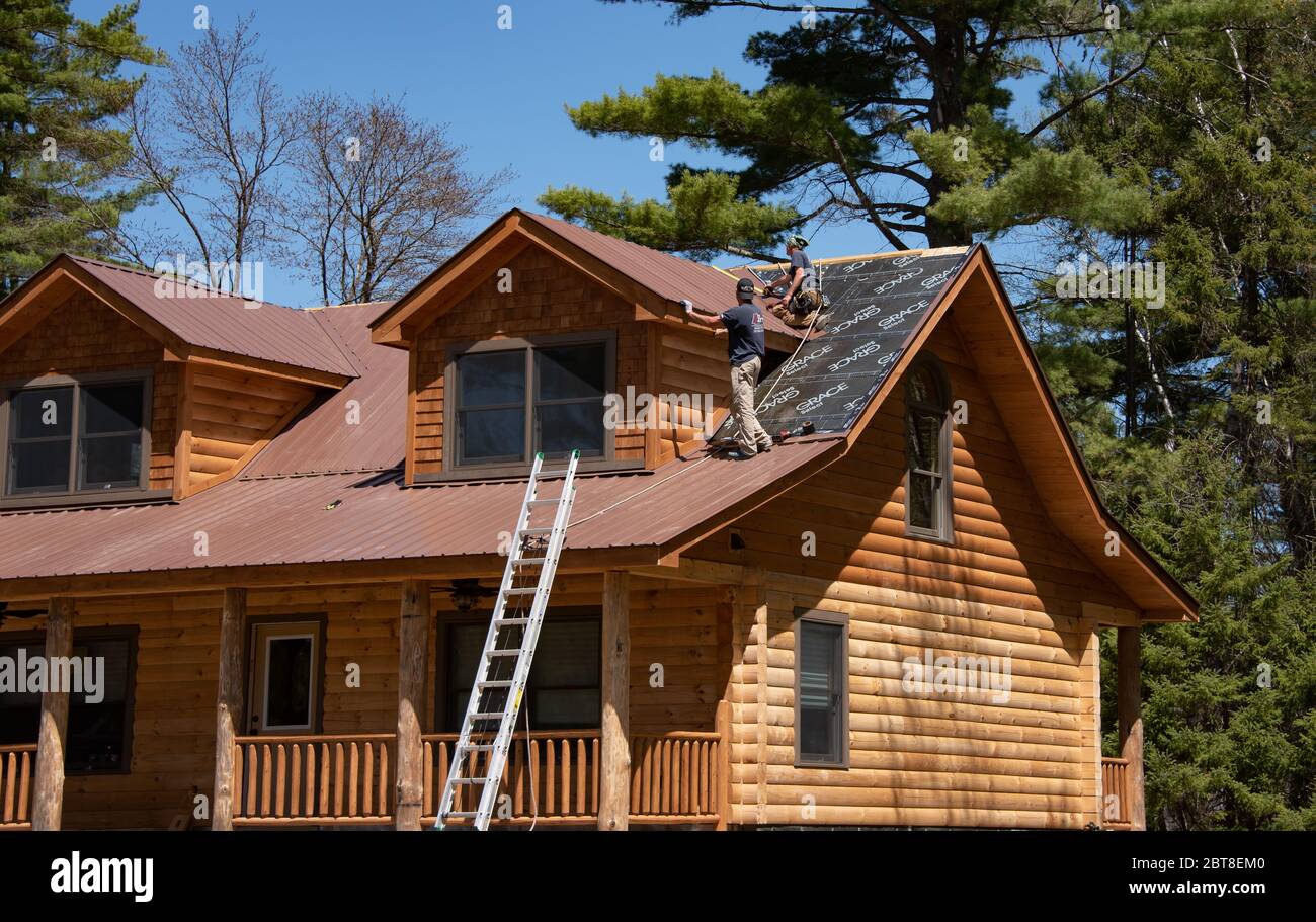Two construction workers installing a metal roof on a newly built log cabin in the Adirondack Mountains, NY USA Stock Photo