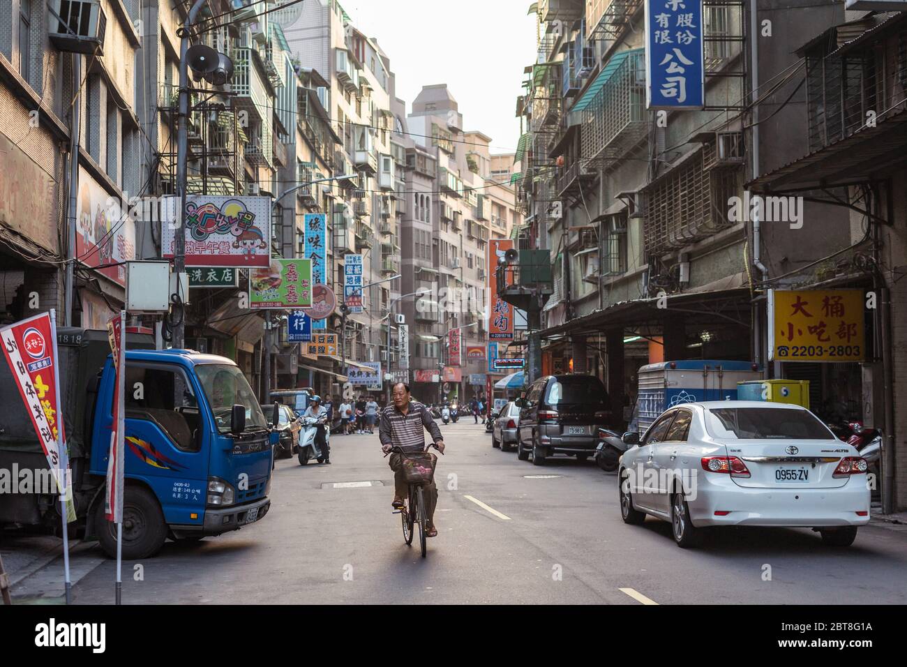Taipei / Taiwan - December 12, 2018: senior man riding bicycle along scenic street with multitude of buildings Stock Photo