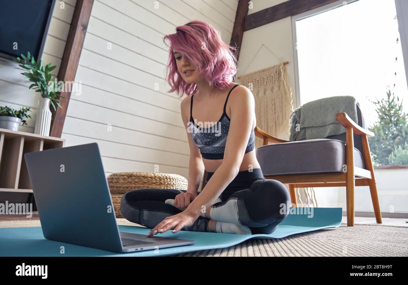 Young fit teen hipster girl pink hair searching online fitness class at home. Stock Photo
