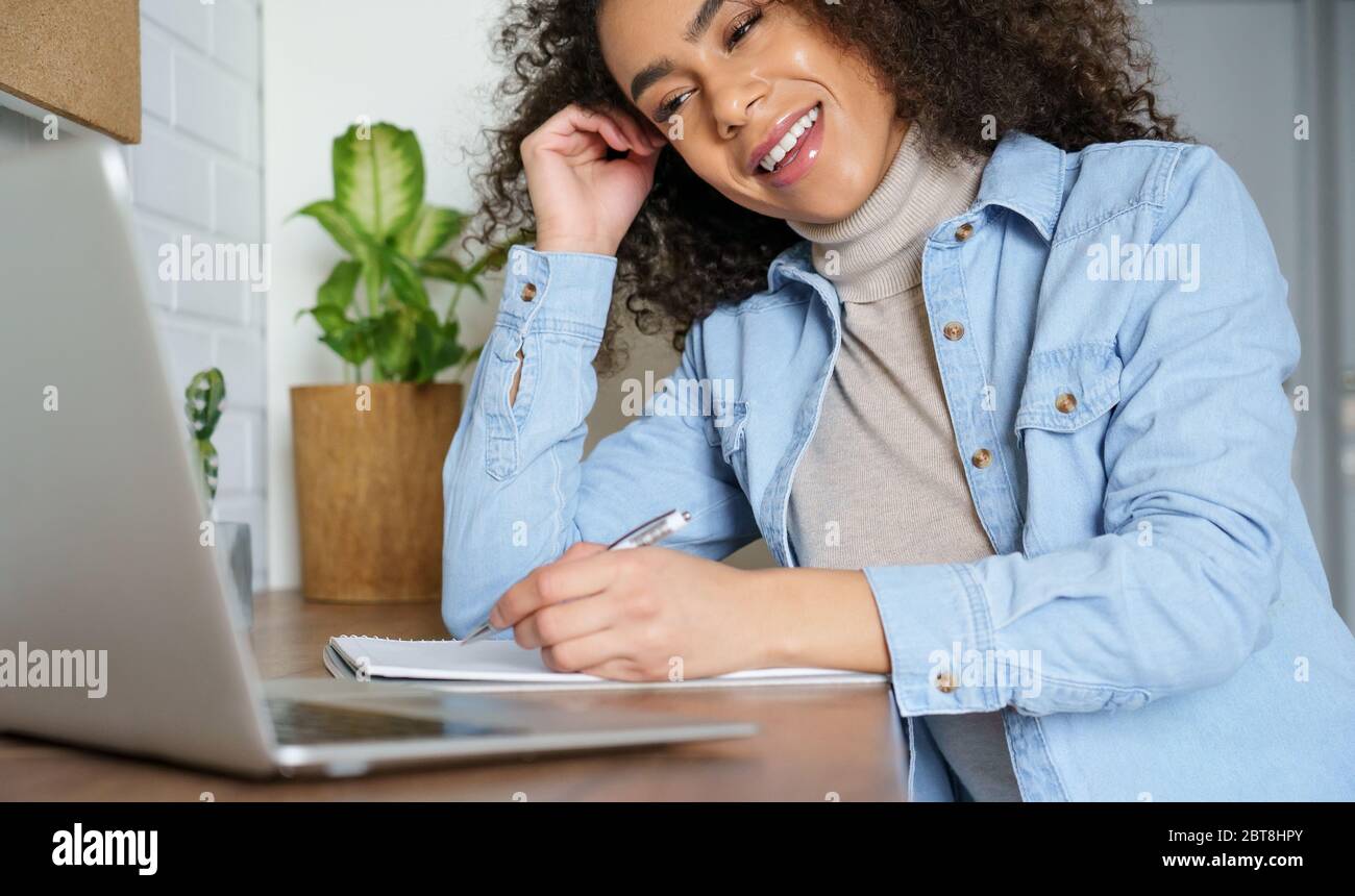 African girl student elearning on laptop making notes work from home office. Stock Photo