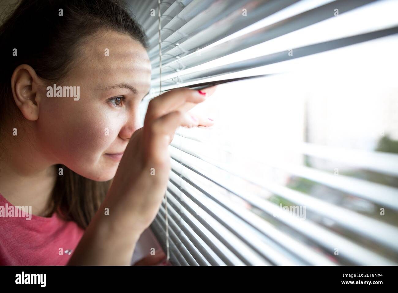 Young brunette woman watching out from the window, stalking, observation concept Stock Photo
