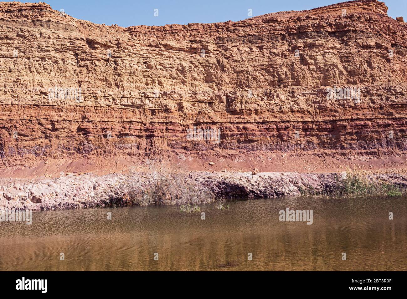 closeup of the geological strata revealed in an old abandoned clay quarry in the makhtesh ramon crater in israel with a pond created by the mining in Stock Photo