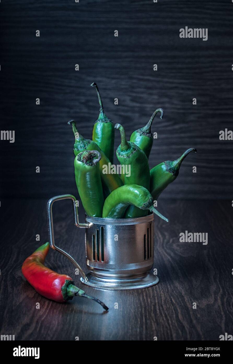 On a wooden table in a metal cup holder are green hot hot peppers Stock Photo