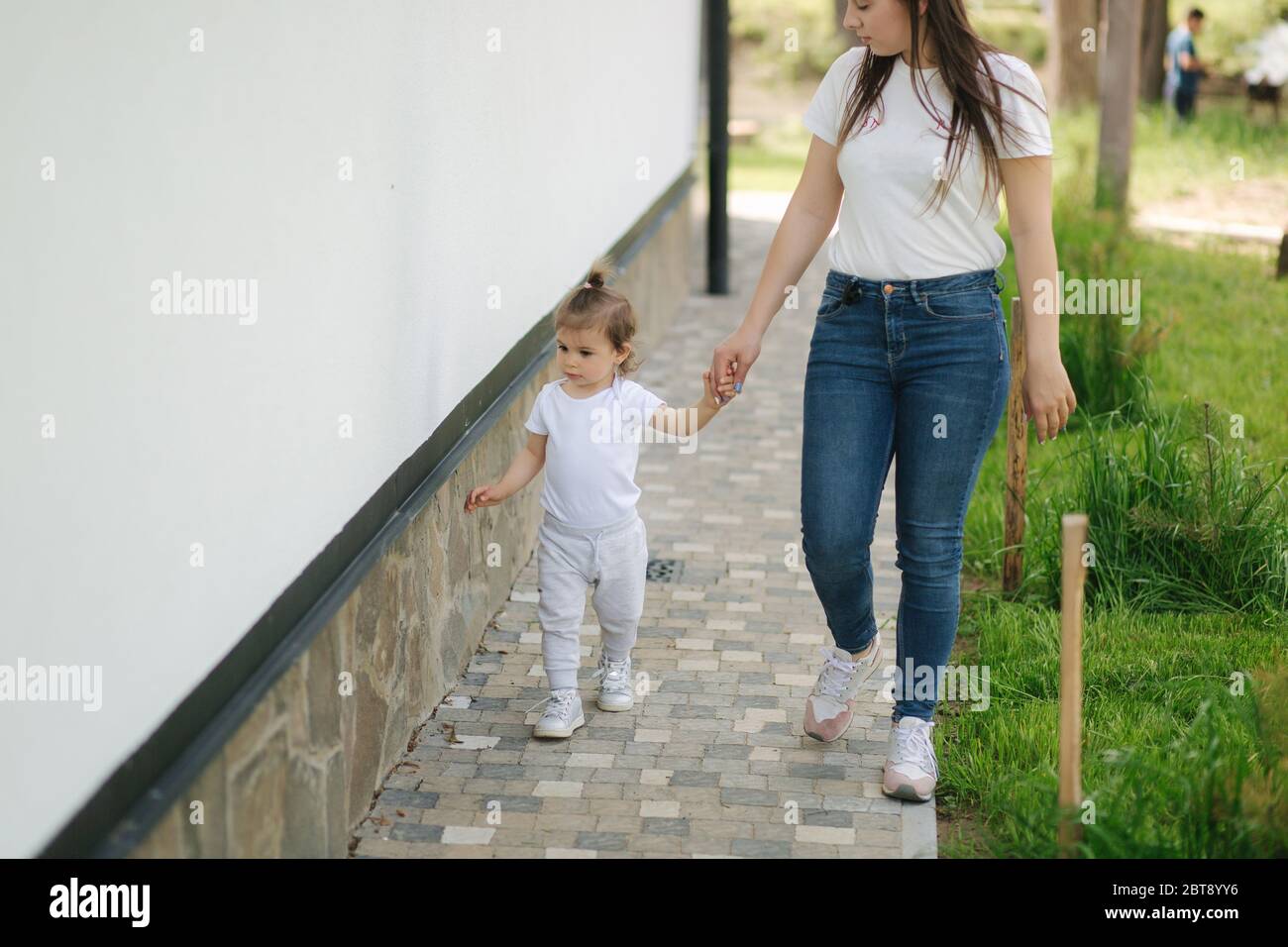 Cute little girl spend time with mom neae the house. Mother and daughter walk on the backyard