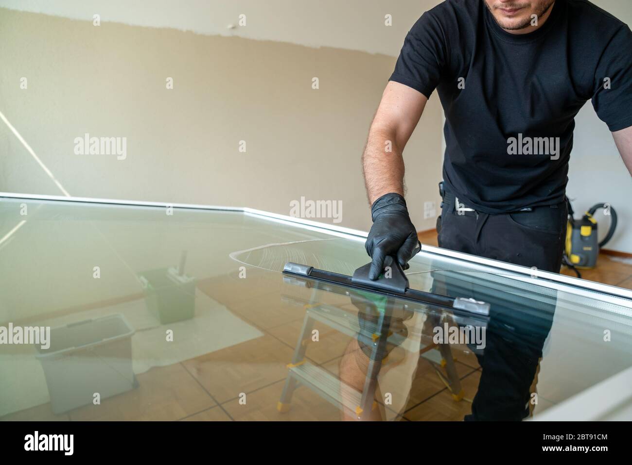 A professional cleaner using a squeegee and scraper to clean a large apartment window Stock
