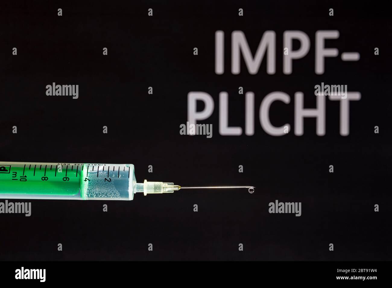 This photo illustration shows a disposable syringe with hypodermic needle, IMPFPLICHT written on a black board behind Stock Photo