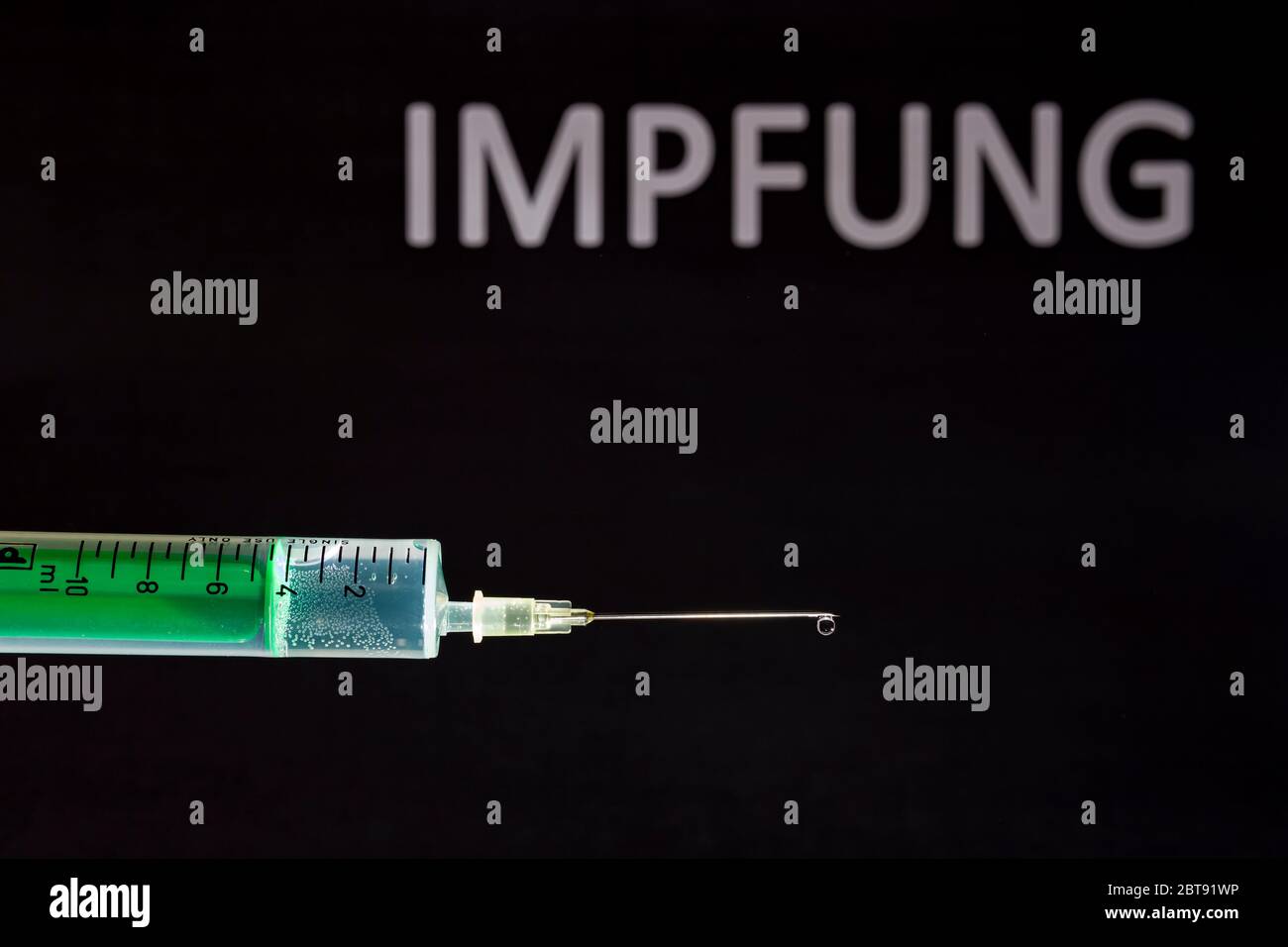 This photo illustration shows a disposable syringe with hypodermic needle, IMPFUNG written on a black board behind Stock Photo