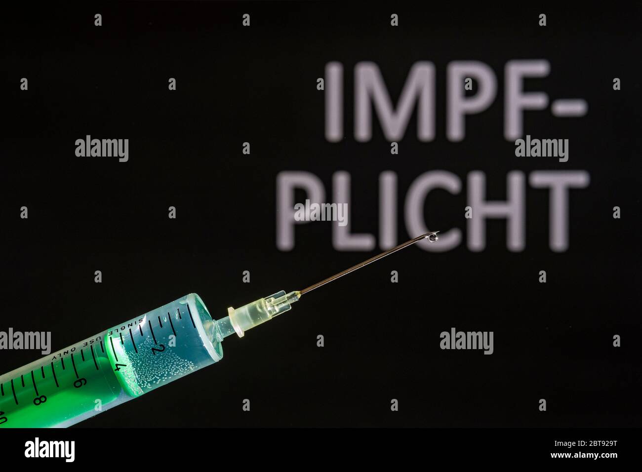 This photo illustration shows a disposable syringe with hypodermic needle, IMPFPLICHT written on a black board behind Stock Photo